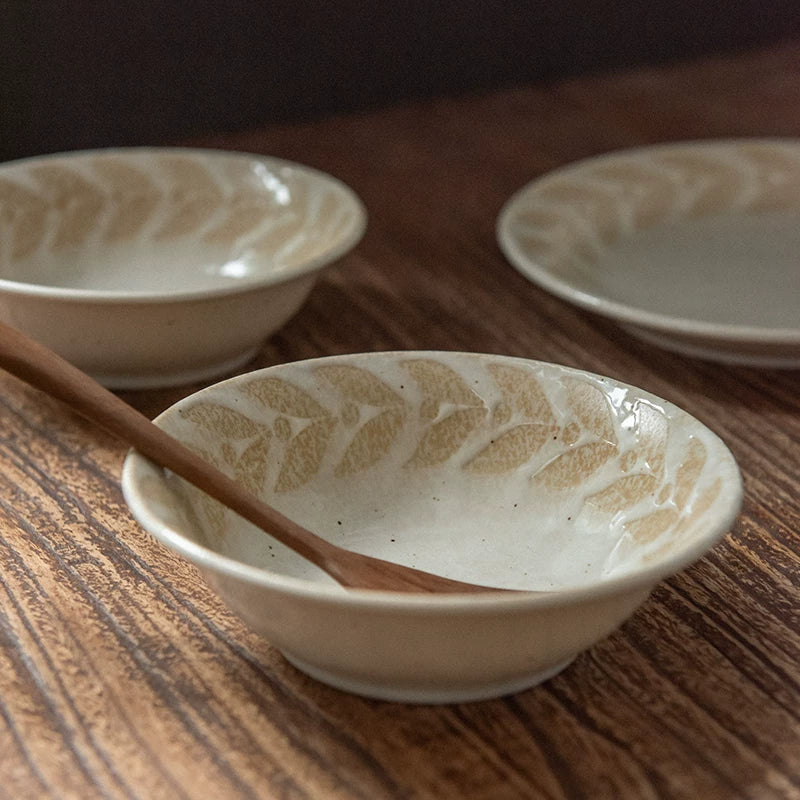 Two shallow ceramic bowls with beige leaf pattern, one holding a wooden utensil.