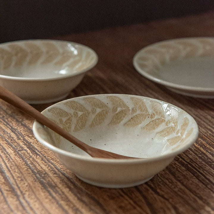 Two shallow ceramic bowls with beige leaf pattern, one holding a wooden utensil.