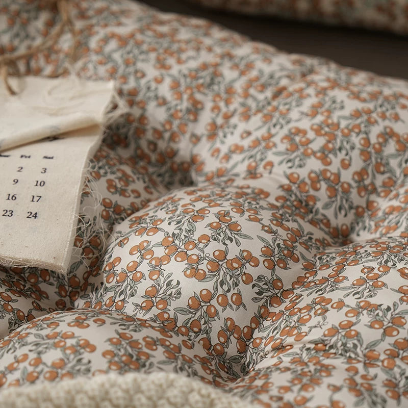 Close-up of a beige floor cushion with an orange berry floral pattern, tufted design.