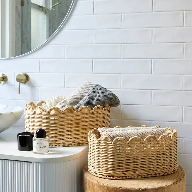 Two natural rattan wicker baskets with scalloped edges.  Beige/tan color,  bathroom setting.  Towels inside.