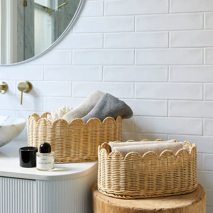 Two natural rattan wicker baskets with scalloped edges.  Beige/tan color,  bathroom setting.  Towels inside.
