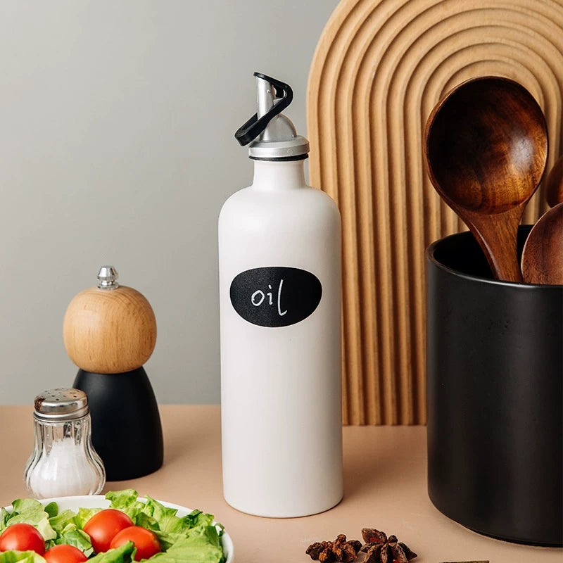 A beige ceramic oil dispenser bottle with a dark brown lid and spout on a white surface.