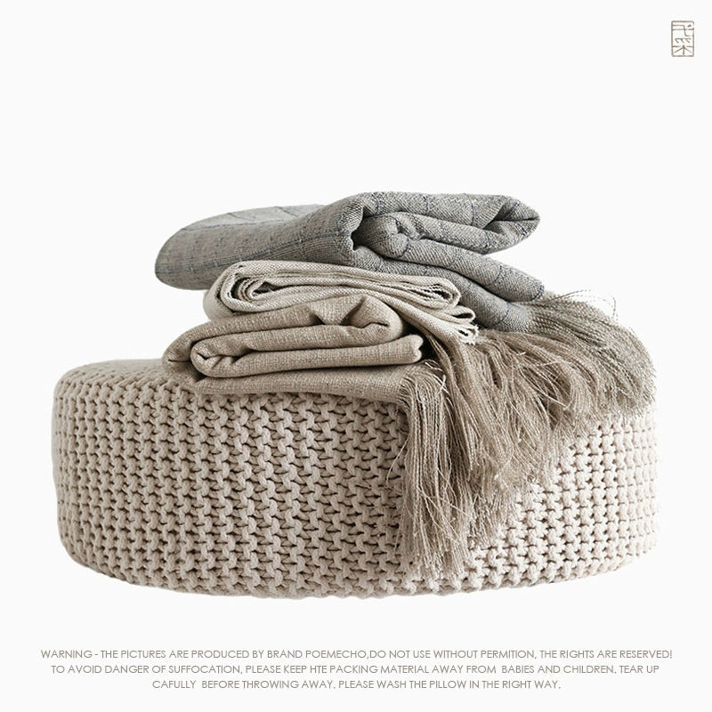 Beige linen table runner with tassels on woven pouf. Rustic decor accent.