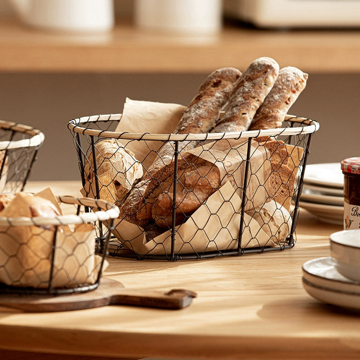 Black wire woven bread basket with beige bamboo border.  Oval shape, filled with assorted breads. Kitchen decor.