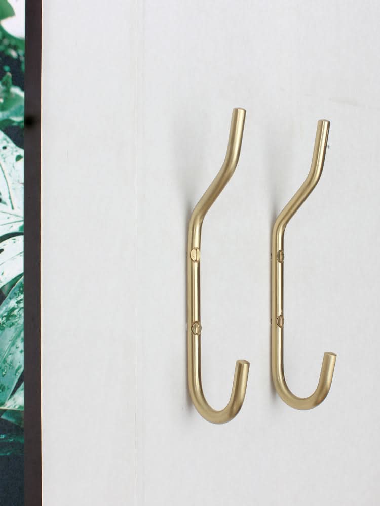 Minimalist brass wall hooks on a white wall, subtle gold finish, home decor essential.