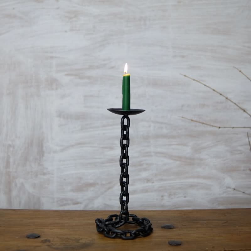 Black chain candle holder with green candle on wooden table, textured background.