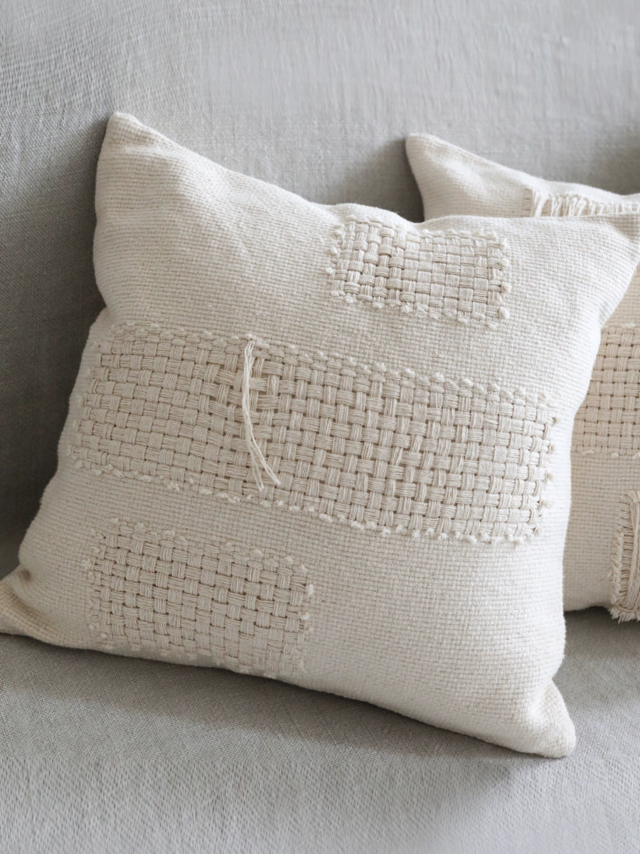 Cream woven throw pillows with modern boho texture on gray sofa.