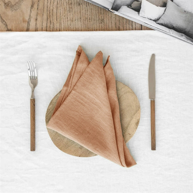 Elegant Linen Table Napkins in rust orange, knotted on a wooden charger, with fork and knife. Set of 4.
