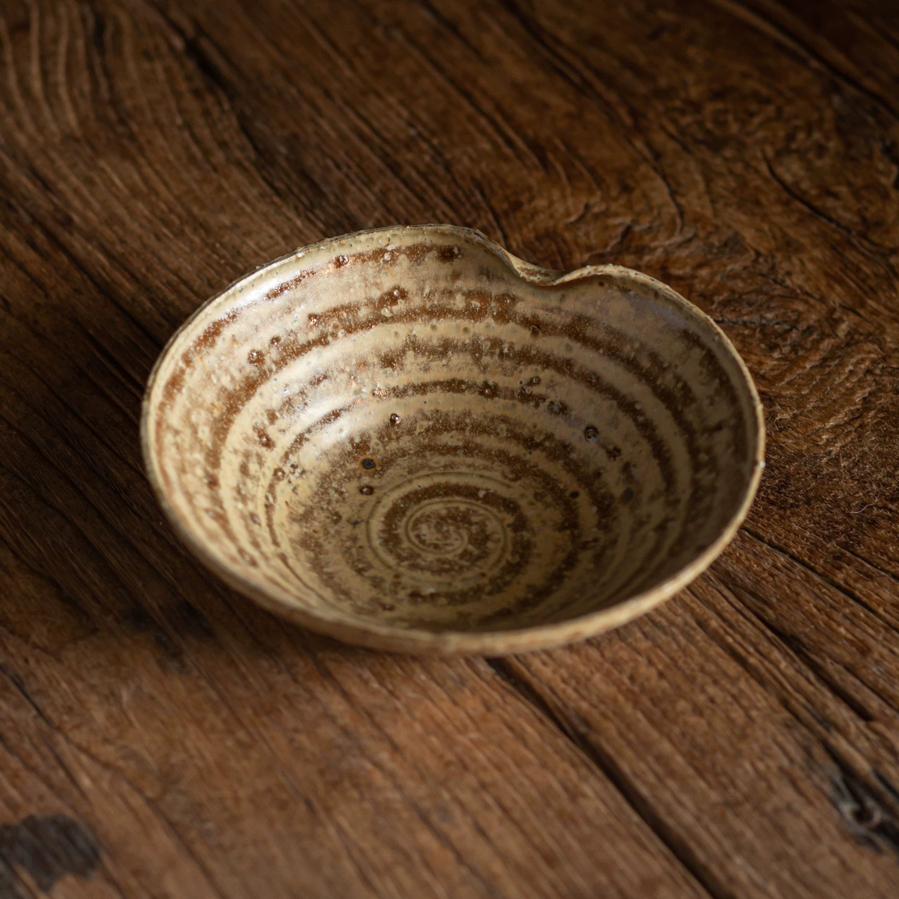 Top-down view of a heart-shaped bowl featuring a light, speckled yellowish-brown reactive glaze on wood.