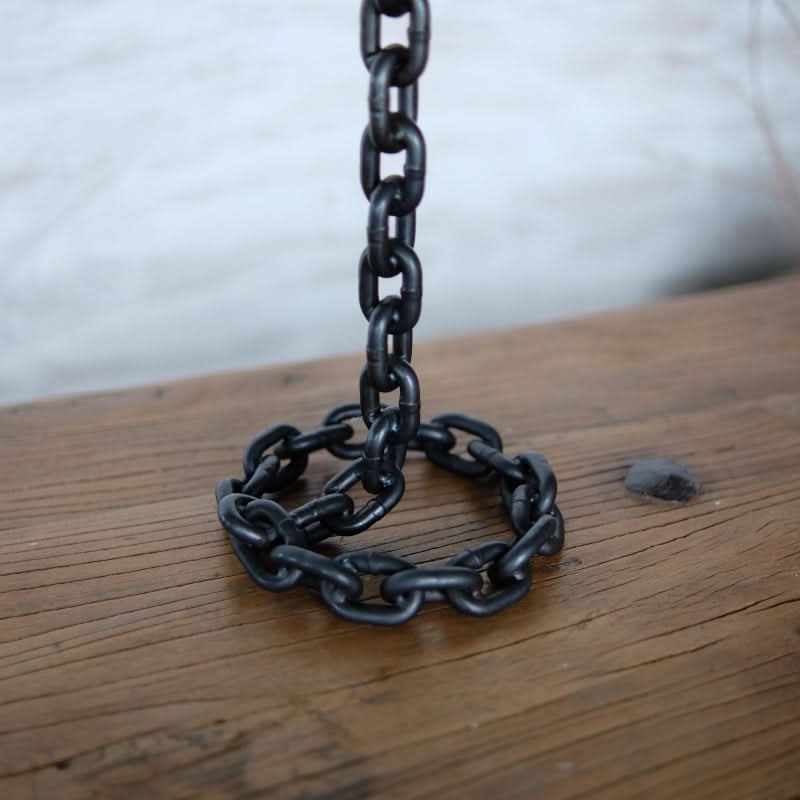 Black metal chain candle holder on rustic wood surface.