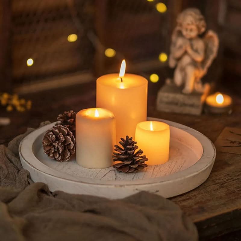Rustic white wooden tray decorative with three glowing pillar candles and pinecones.
