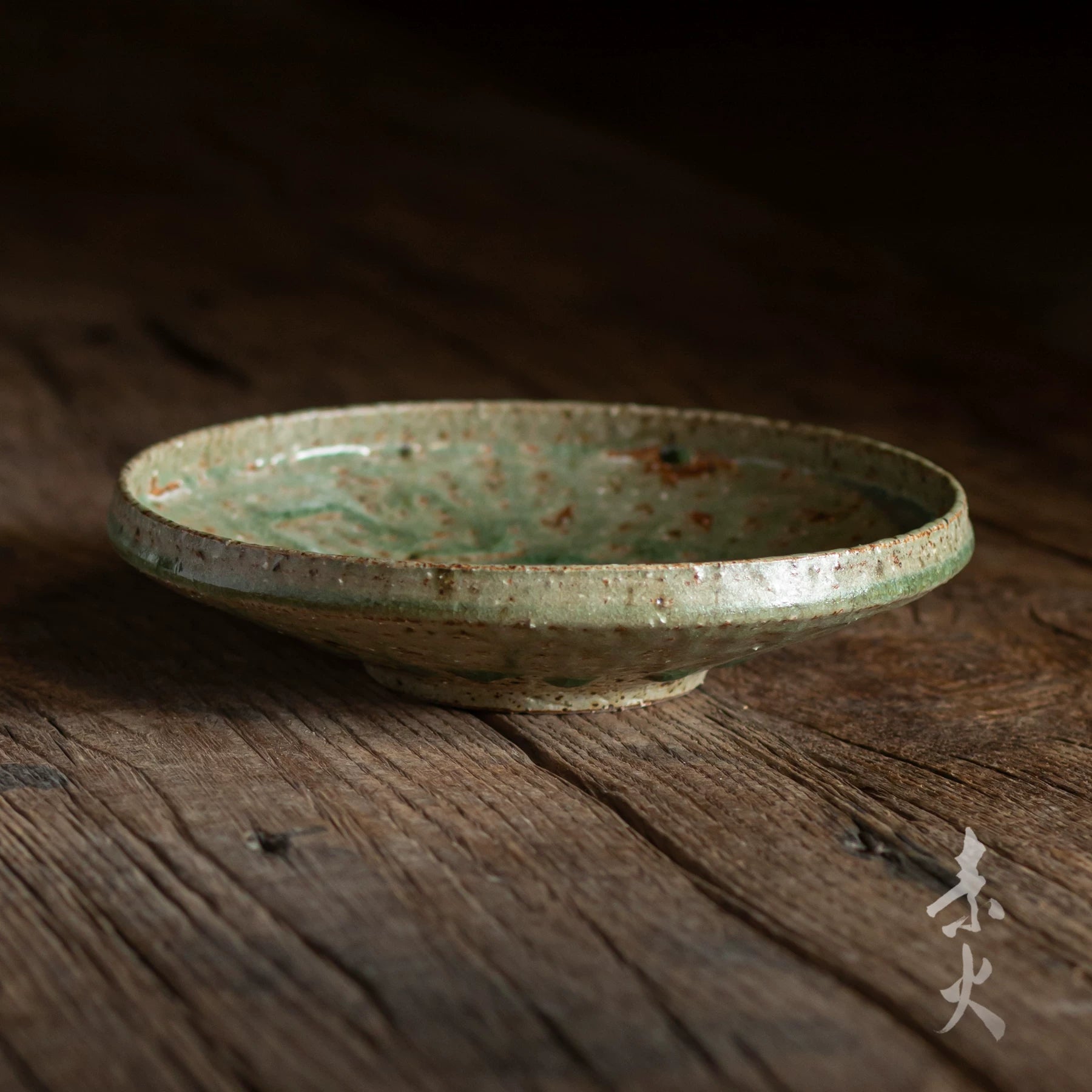 Single ceramic footed serving plate with speckled green glaze sitting on a dark wooden surface.