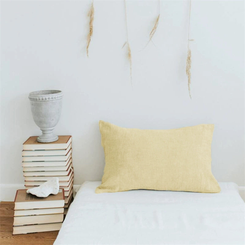 Pale yellow linen pillow case with frills, displayed on a white surface next to stacked books and a vase.