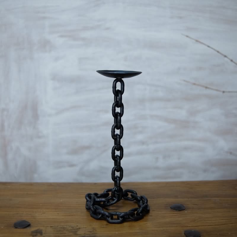 Black metal chain candle holder on wooden table, industrial home decor accent.