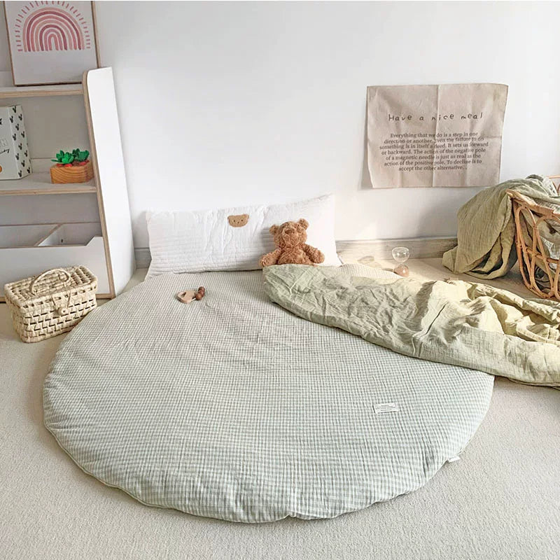 Round light green and white gingham play mat with a teddy bear and light green blanket.