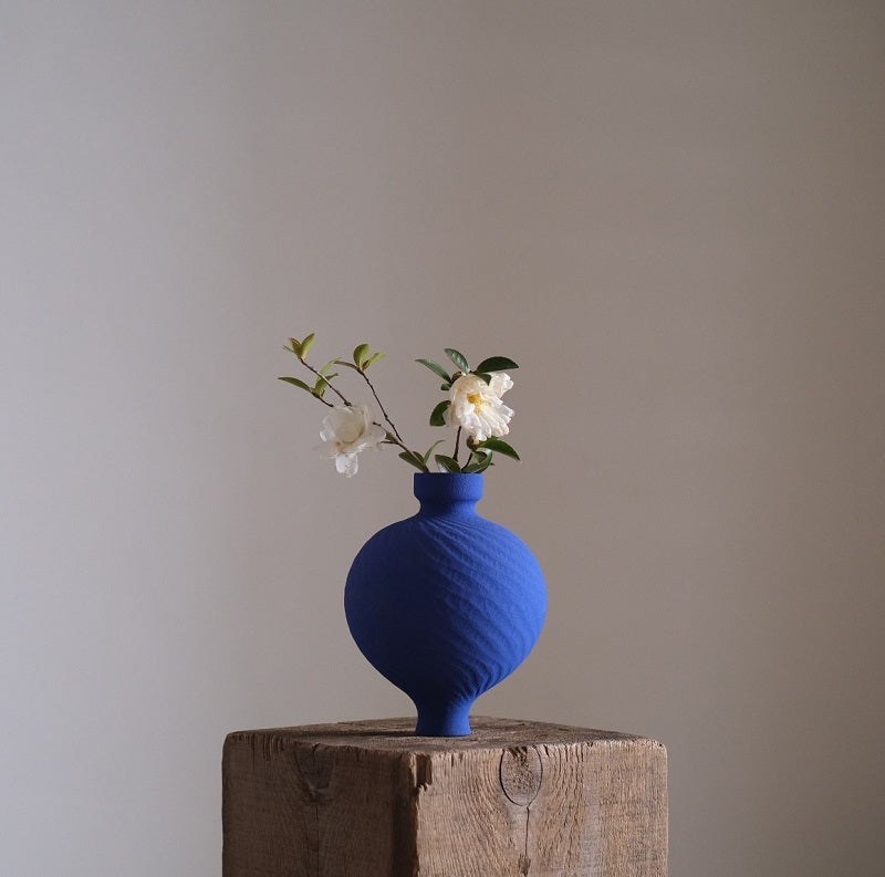 Klein Blue Flower Vase, handcrafted ceramic with white flowers on a rustic wooden block.