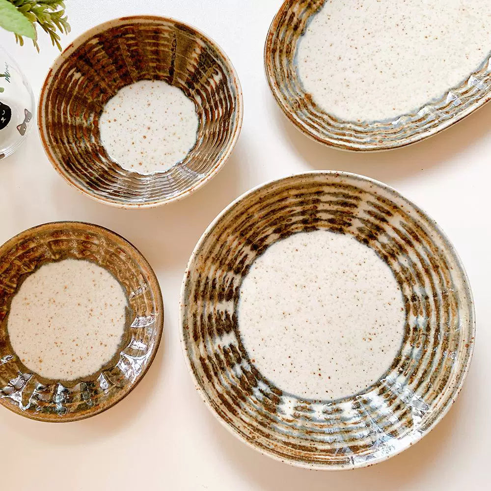 Assortment of rustic ceramic bowls and plates with speckled white centers and brown concentric line patterns.