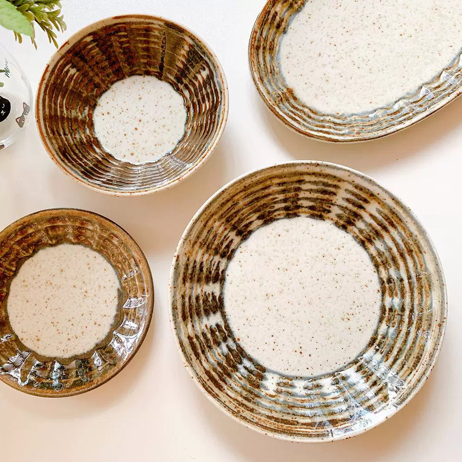 Assortment of rustic ceramic bowls and plates with speckled white centers and brown concentric line patterns.