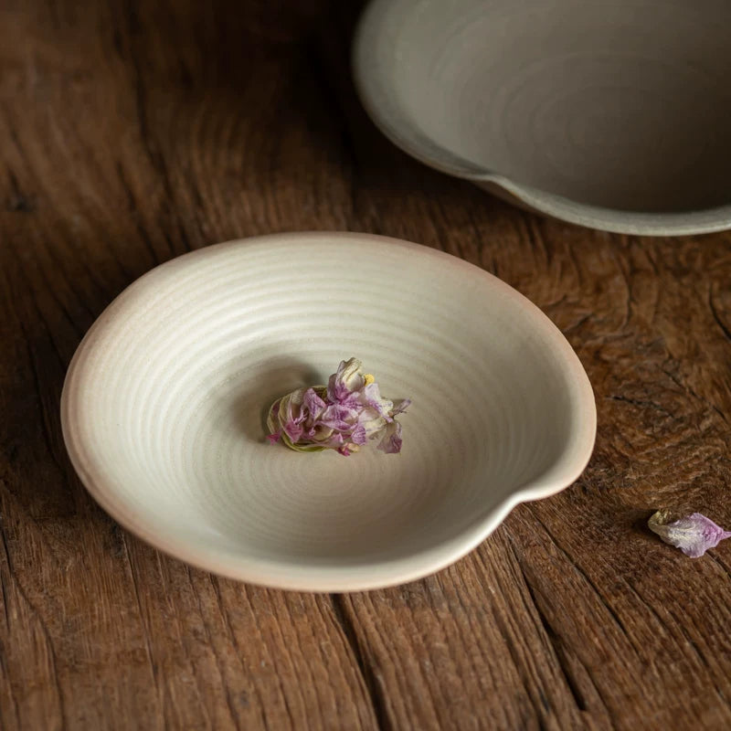 Light cream-colored ceramic saucer with a small indentation, featuring spiral texture and dried flowers.