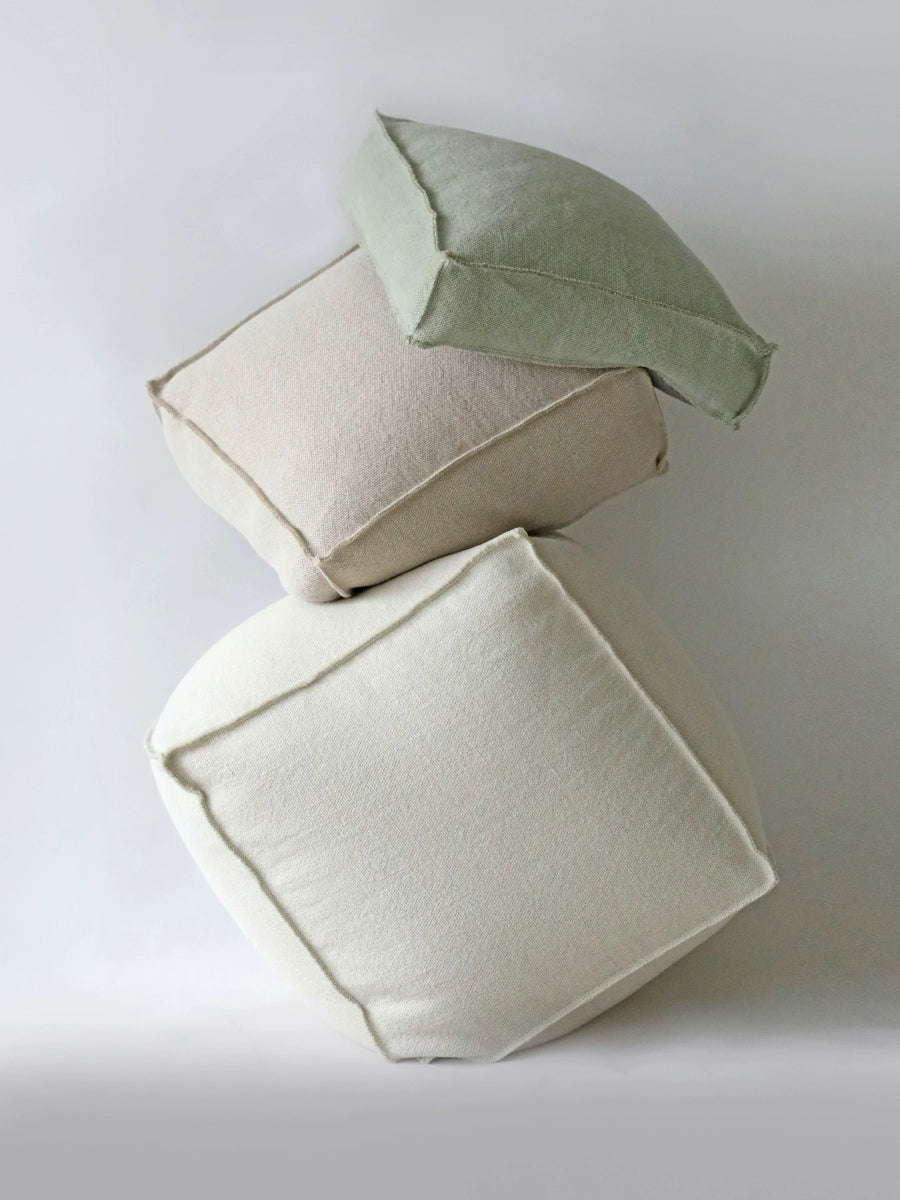 Stacked knitted poufs in beige and sage green.  Square shape, visible stitching.  Modern, neutral colors.