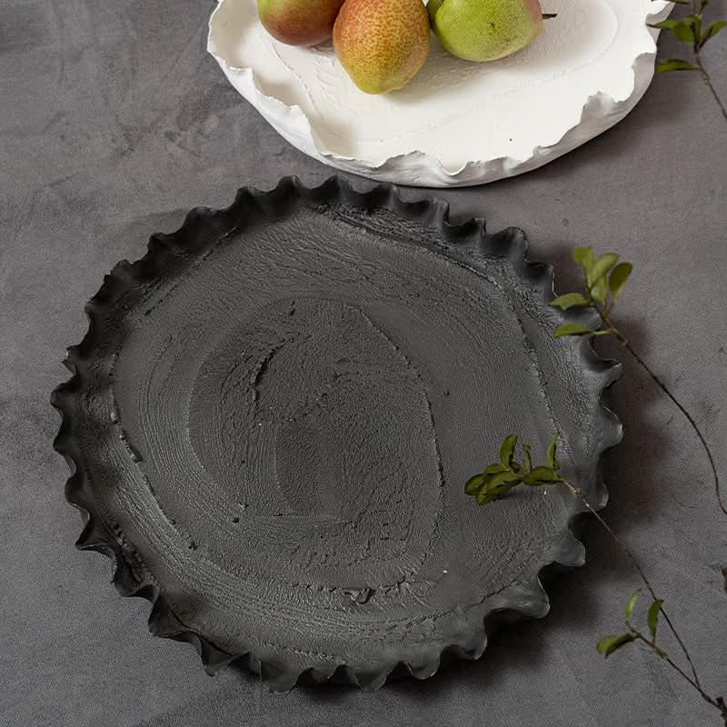 Wabi-sabi ceramic serving dish in charcoal grey with ruffled edge, on a grey textured surface.