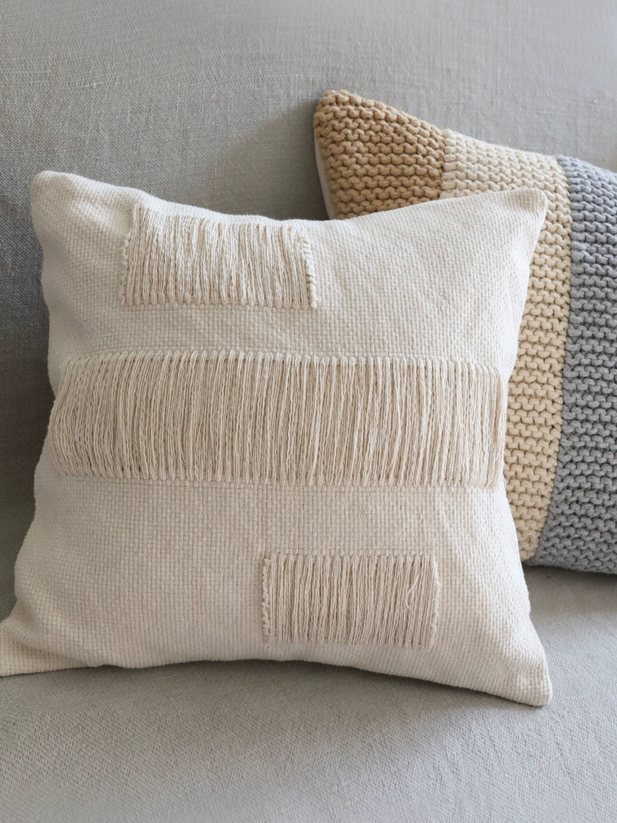 Cream woven throw pillow with fringe details, set of 4, on a light gray couch.