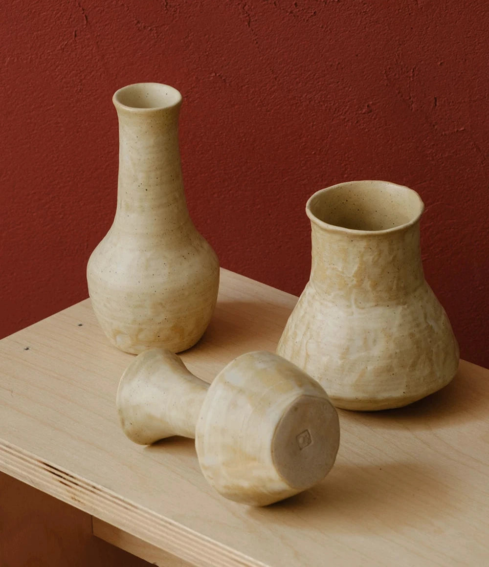 A small, hand-thrown ceramic vase with a textured, creamy white curd glaze and a narrow neck.