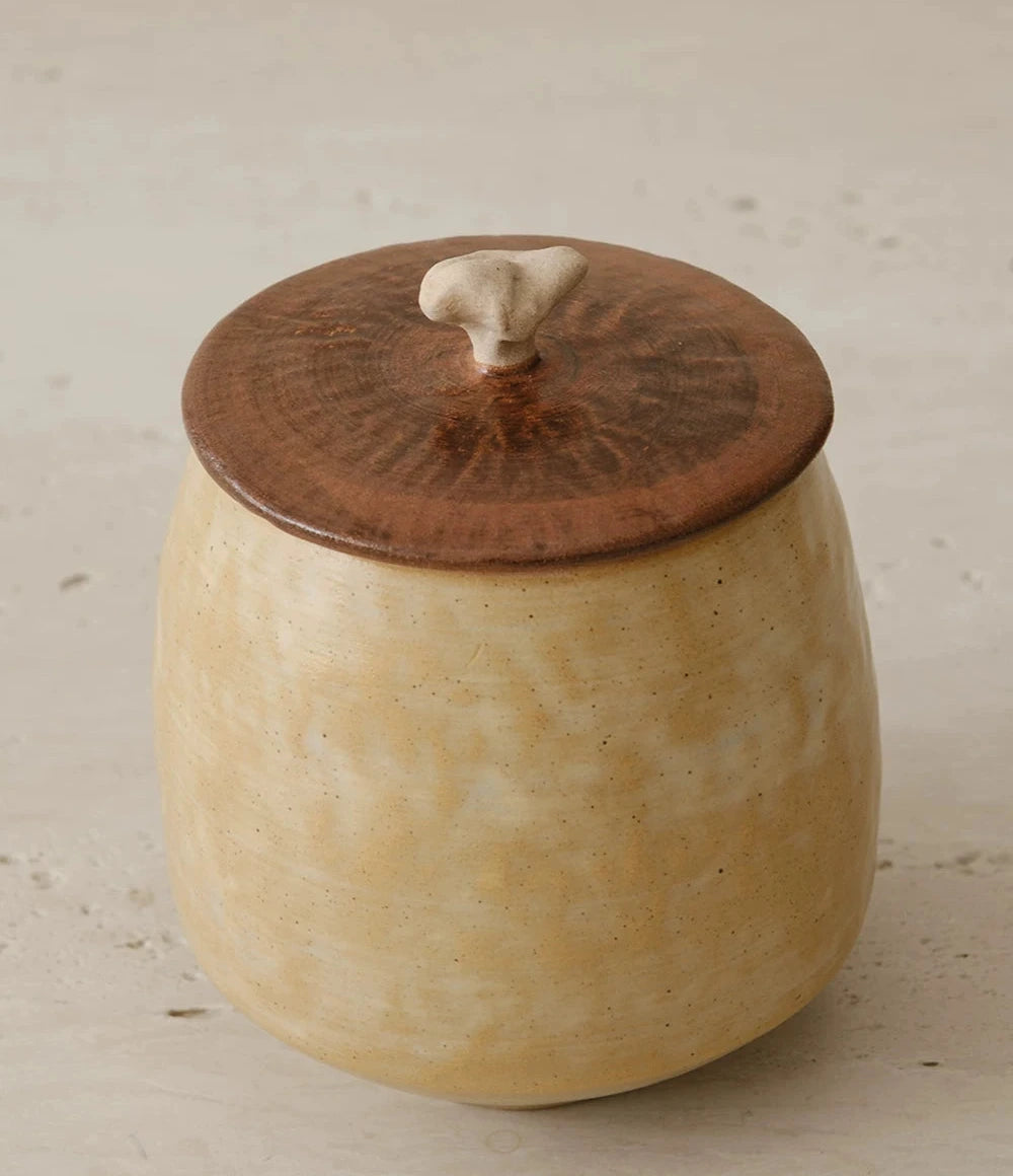 A textured white ceramic storage jar with a natural wooden lid sits against a plain background.