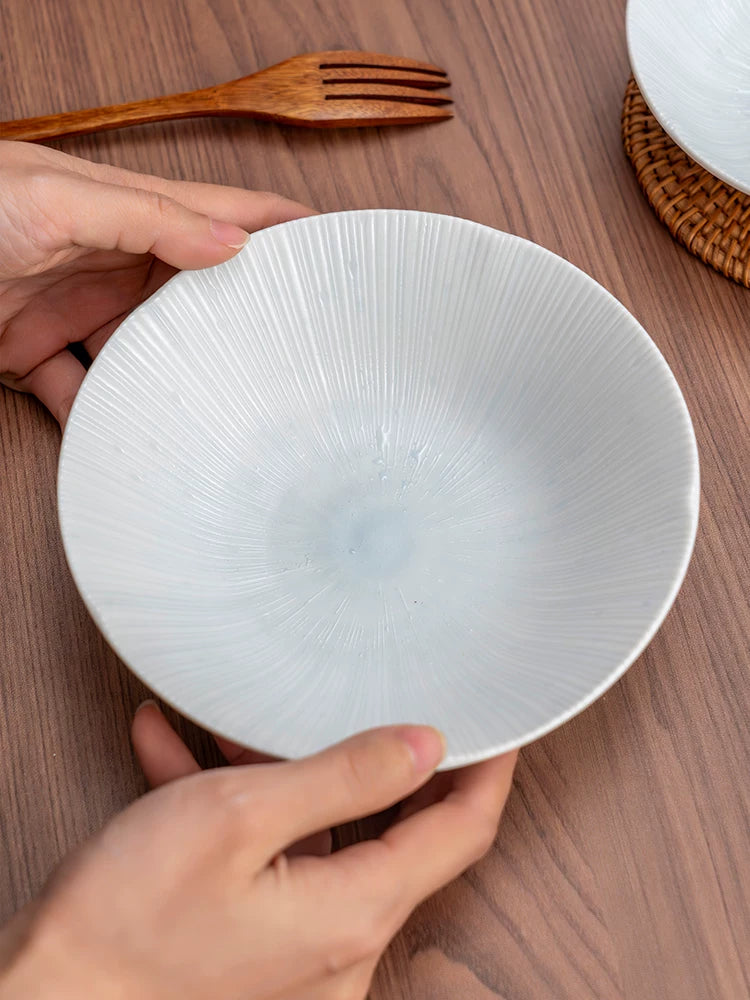 Hands holding a large white ceramic plate with fine radial texture, detailed close-up.