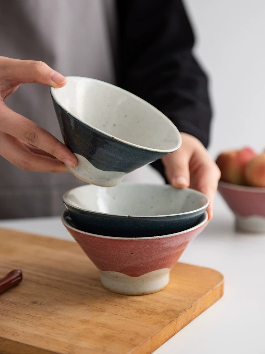 Hands stacking two ceramic bowls, one dark blue and one dusty pink.