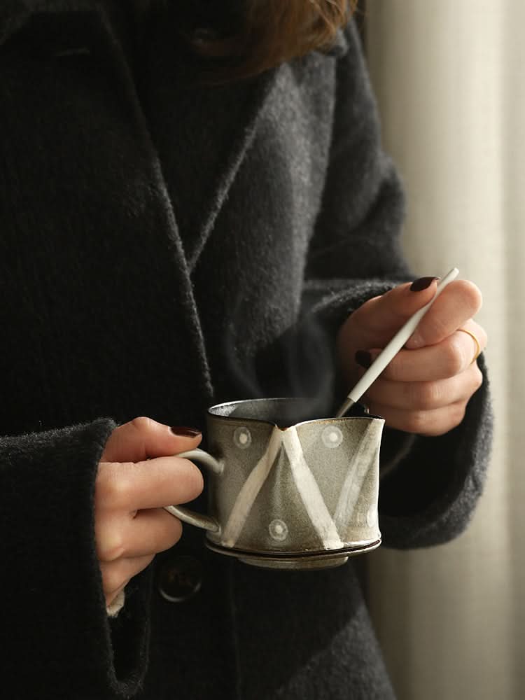 Rustic handcrafted coffee cup with unique geometric pattern, held by person in coat.