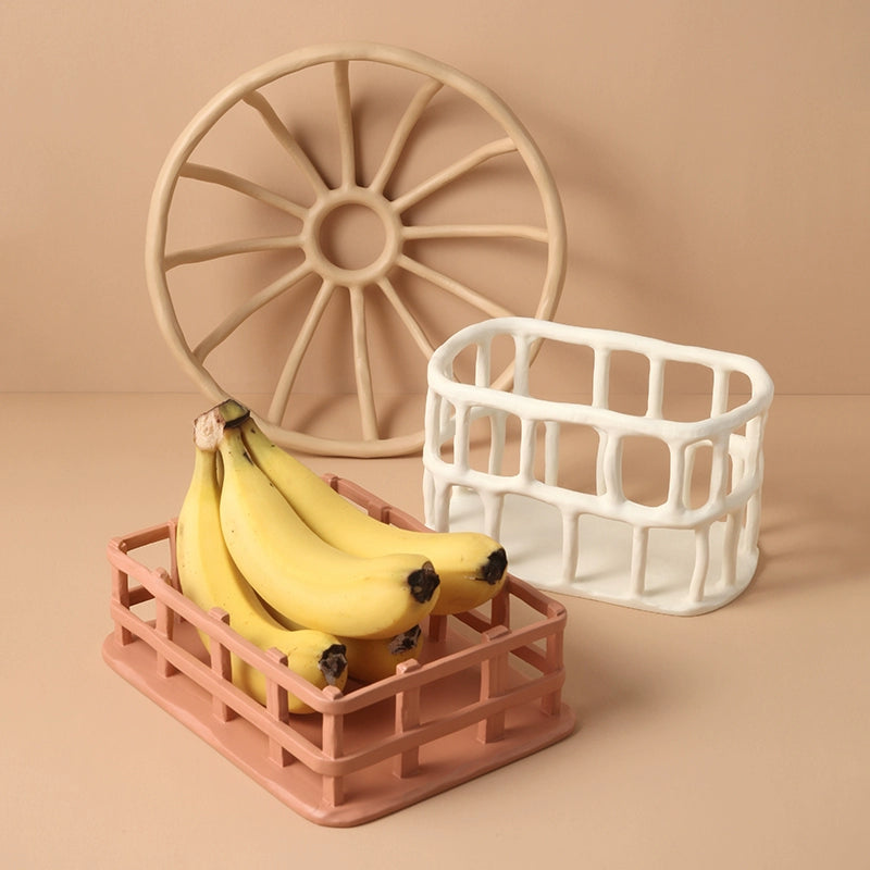 Hand-carved ceramic fruit basket, beige/peach, openwork design, rectangular shape, holding bananas.  Beige/peach colored basket with a decorative openwork pattern.