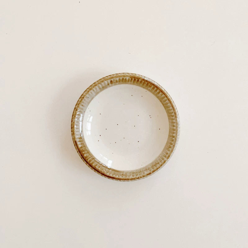 Small round ceramic plate or shallow bowl with speckled white interior and textured brown edge.