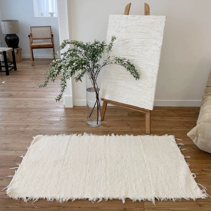 Beige knitted throw blanket, boho style, with frayed edges, on light brown wooden floor.