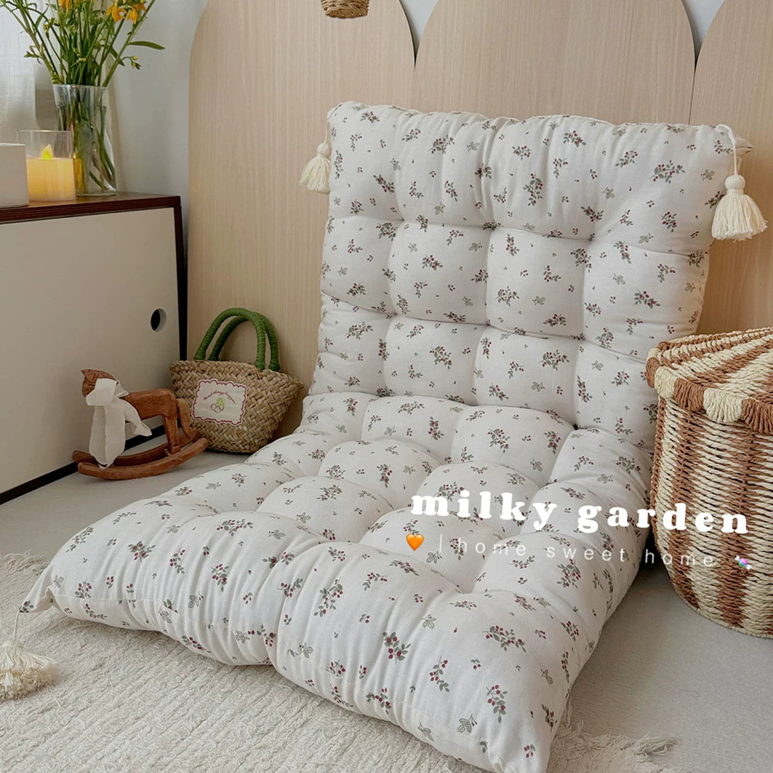Floor cushion with small brown floral print folded upright as a low-back chair on a rug.