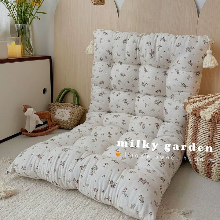 Floor cushion with small brown floral print folded upright as a low-back chair on a rug.