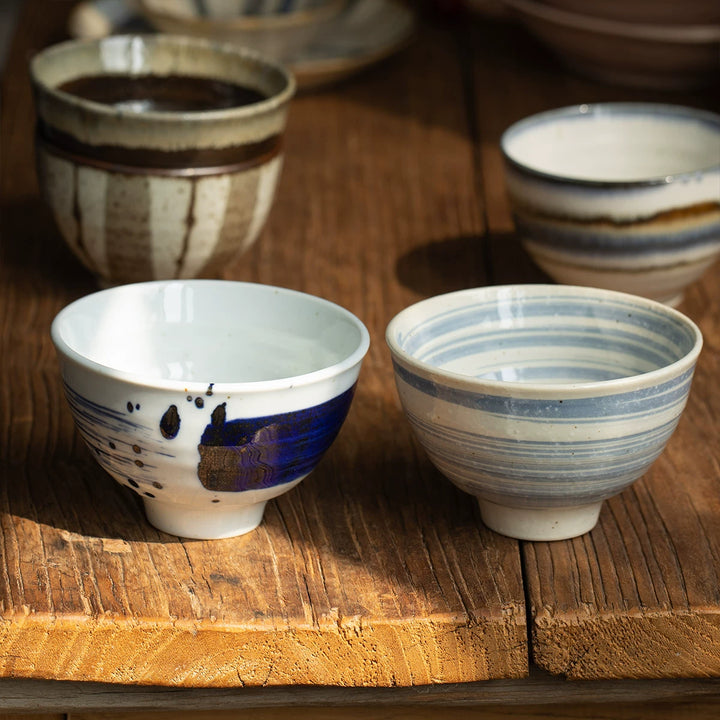 Assortment of Japanese-style ceramic rice bowls with varied rustic glazes on a wooden surface.