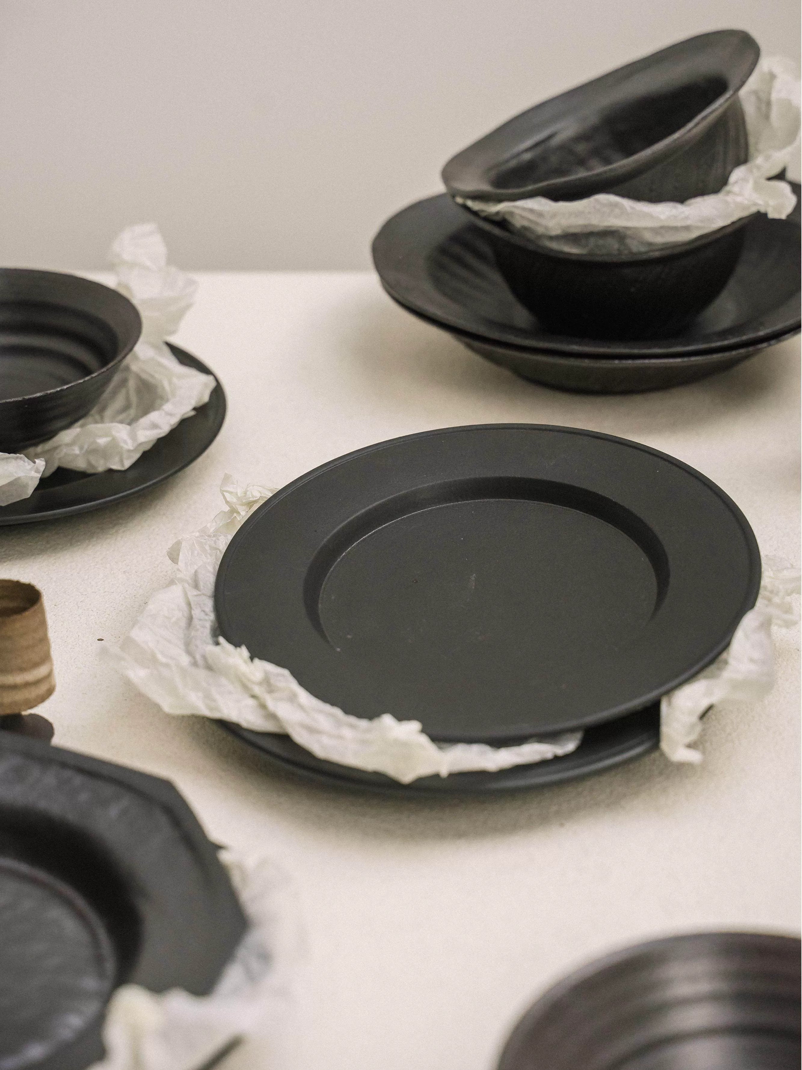Set of matte black dinner plates and bowls stacked with white paper separators
