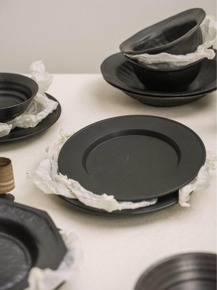 Set of matte black dinner plates and bowls stacked with white paper separators