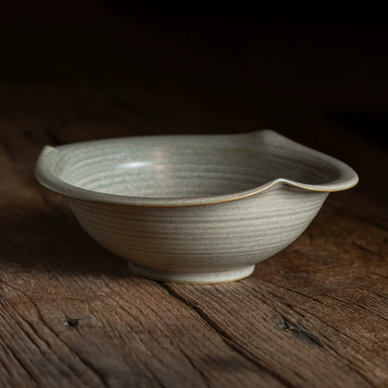 Close-up of a medium-sized, light grey-green ceramic bowl with an angular, wavy rim.