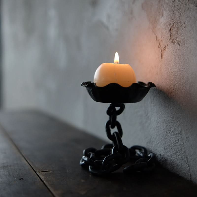 Rustic Candle Holder with Chain Design, black metal, on dark wood table, near textured wall.