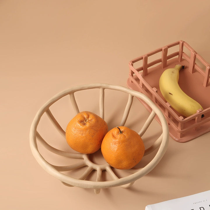 Beige/peach hand-carved ceramic fruit basket with openwork design; two oranges inside.