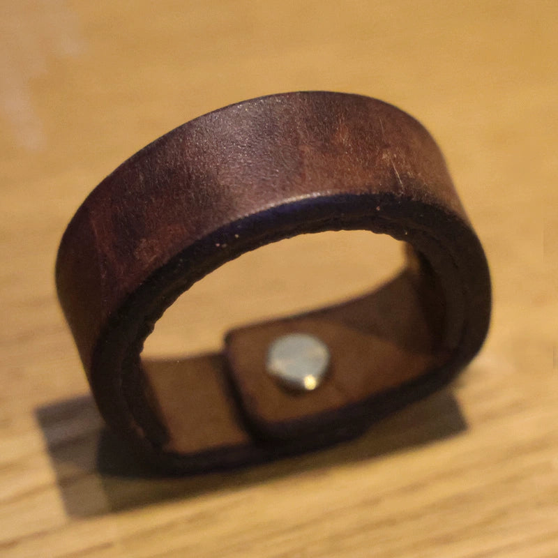 Rustic brown leather drawer pulls with metal fastener on wood surface.