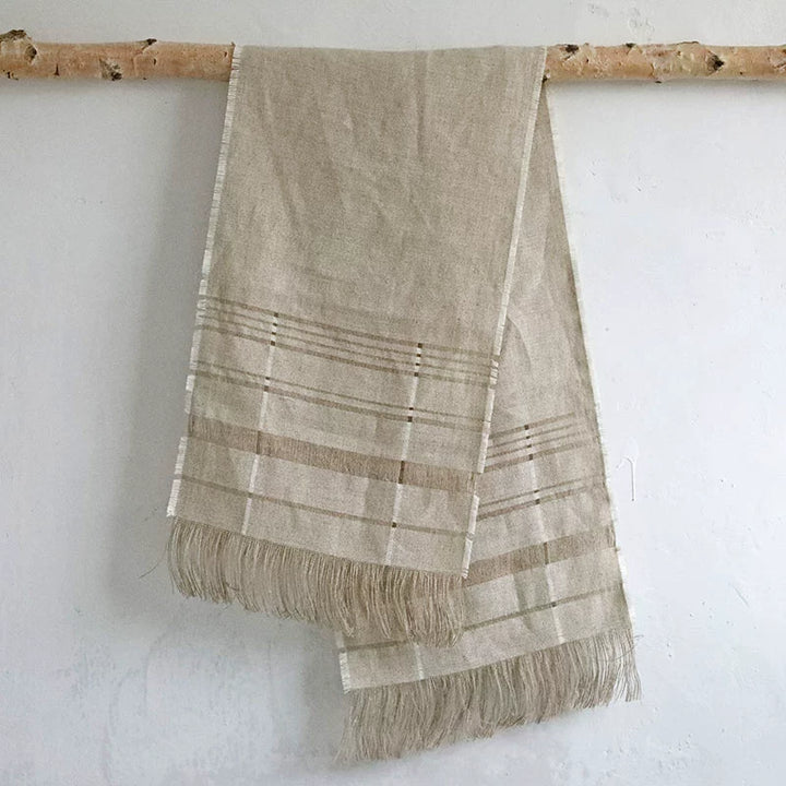 Natural beige linen table runner with fringe and horizontal stripes.
