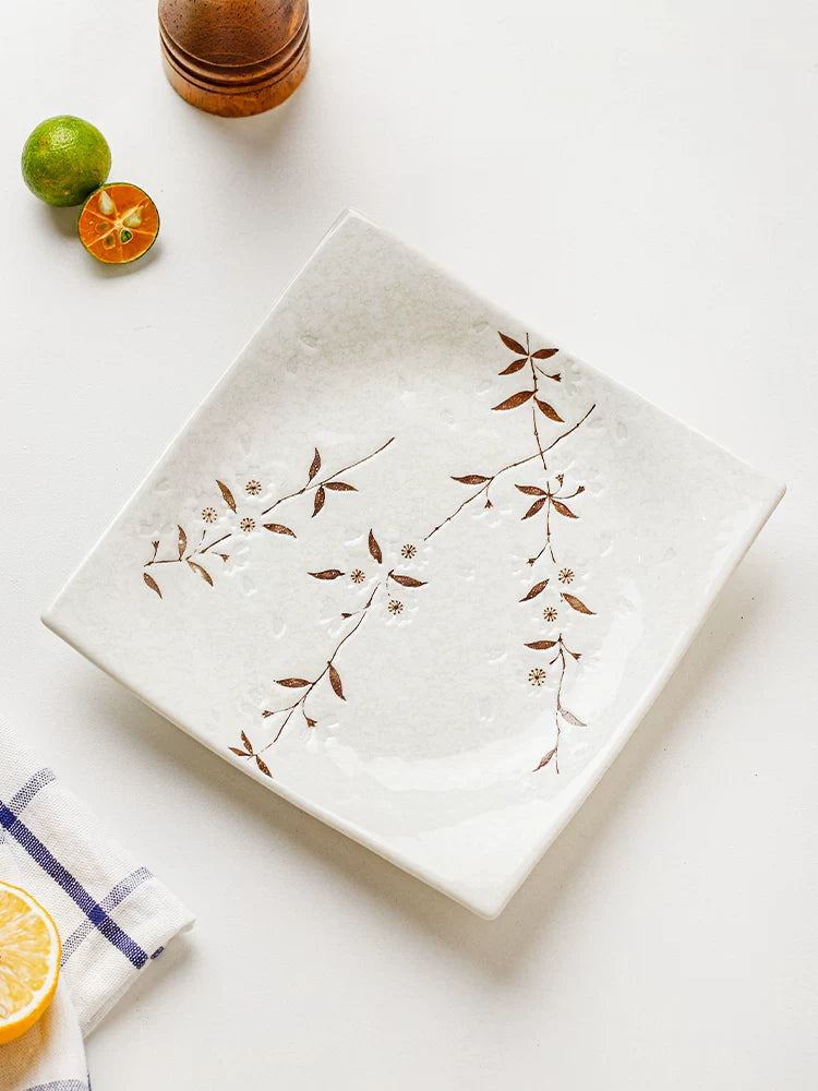 White square ceramic plate with brown cherry blossom motif on a white surface with a napkin.