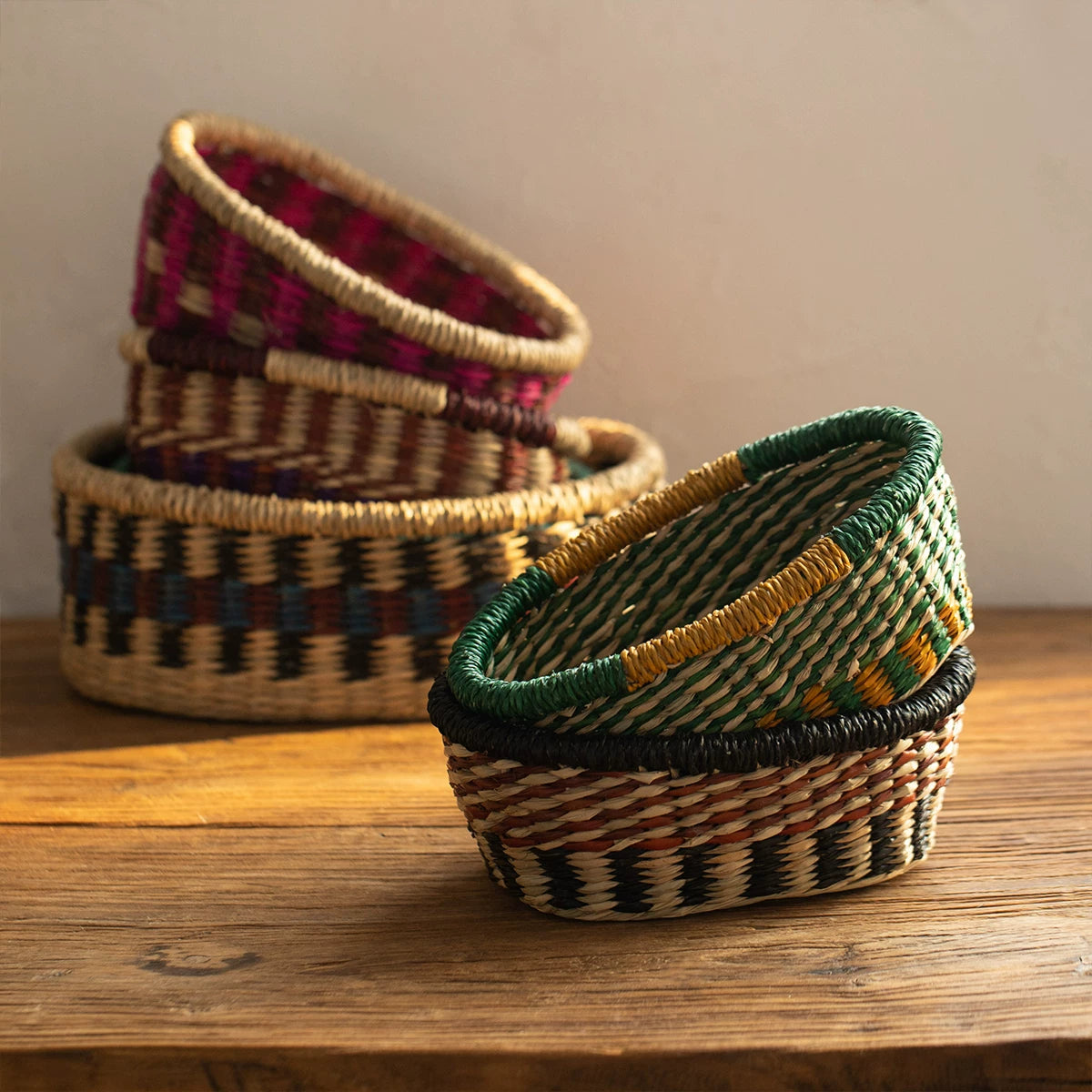 Close-up of stacked seagrass boat-shaped baskets in yellow-green and maroon colors on a wooden table.