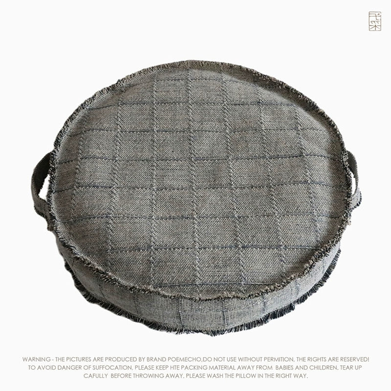 Round beige fabric ottoman pouf with textured grid pattern and side handles.