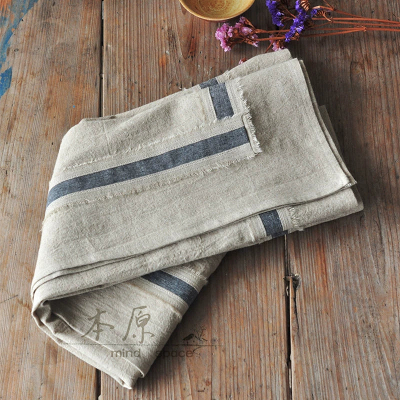 Rustic linen tablecloth in natural beige with blue stripes, farmhouse style, on wooden table.