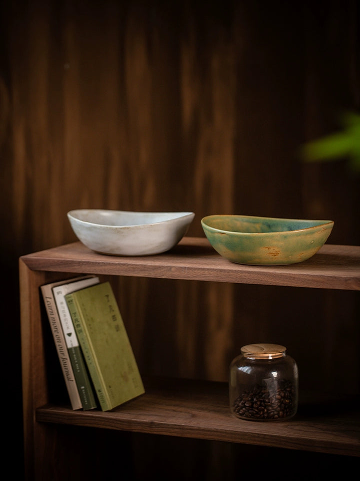 Two hand-painted ceramic bowls, light gray and teal-green, oval shape, rustic style, on wooden shelf.