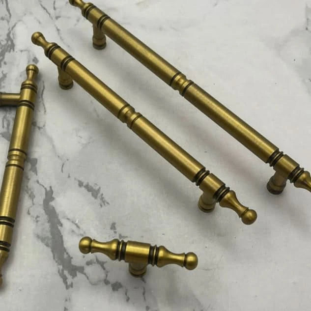 Classic style solid brass cabinet handles with ornate detailing on a marble surface.